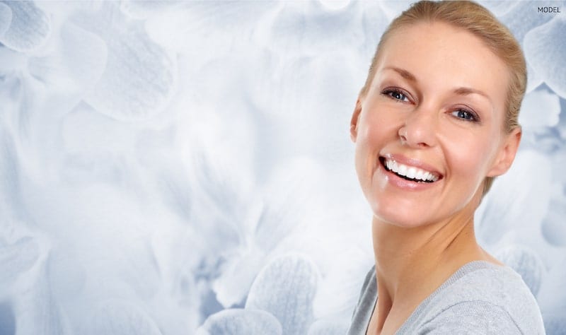 Smiling woman with pulled back hair standing in front of a blue, petal-like background.