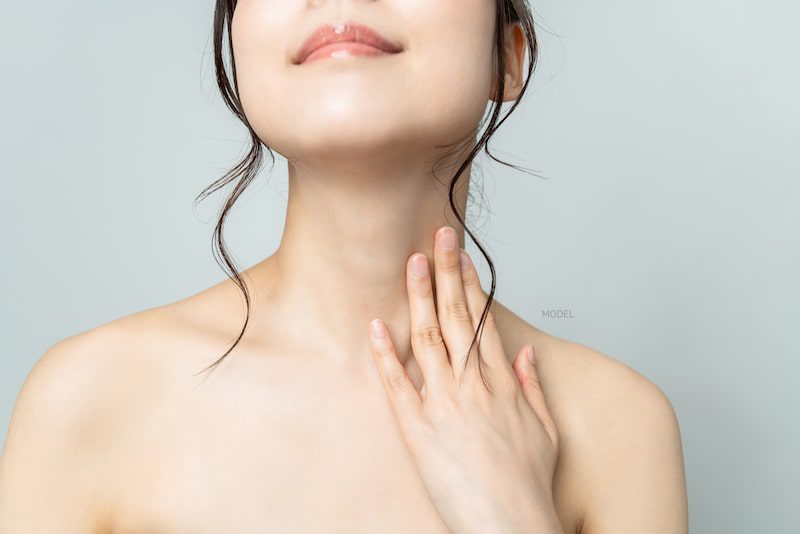 Close-up image of Asian woman's neck with her hand caressing her neck contours.