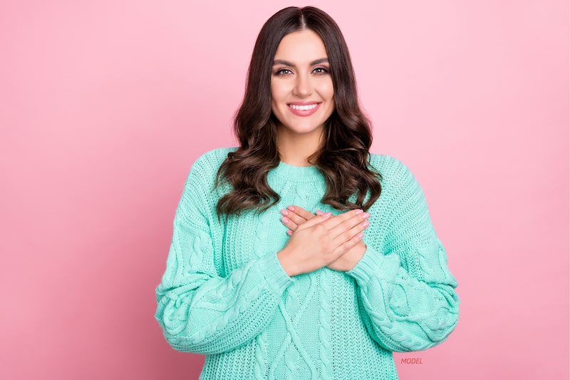 Woman with her hands over her breast against pink. 