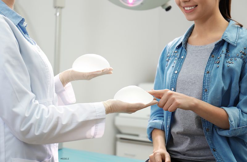 Woman touching a silicone breast implant next to a doctor.