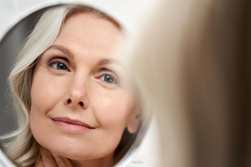 Beautiful middle-aged woman looking at her face in the mirror