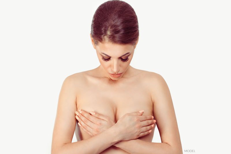 Woman covering naked breasts with her hands.