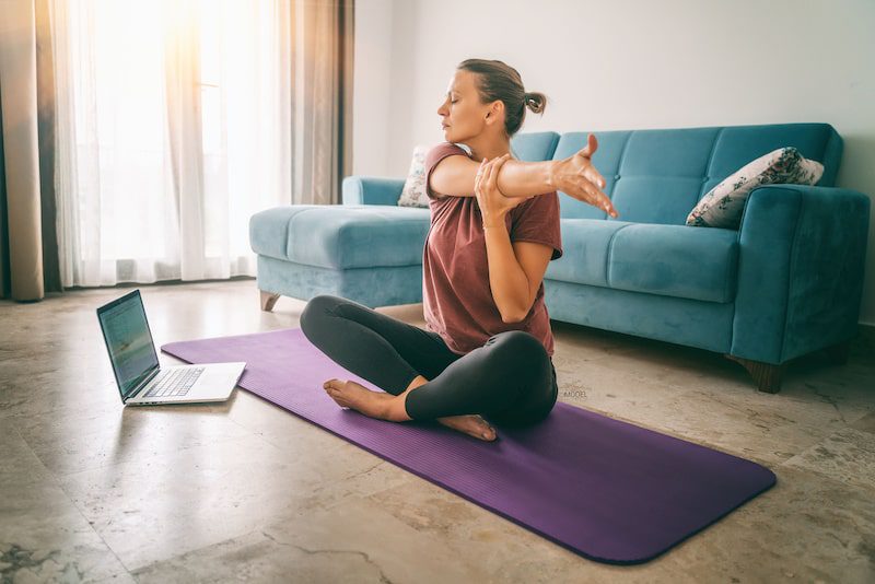 Attractive woman stretching her arm while sitting on a yoga mat.